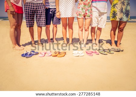 Group of friends on the beach with colored slippers on the sand - Tourists on vacation on a tropical beach during summertime