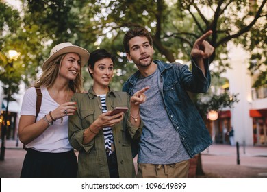 Group Of Friends On City Tour Using Mobile Phone For Navigation. Three Young People Exploring A City Using Smart Phone Gps.