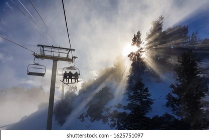 Group of friends on a snowboarding trip to Copper Mountain ride the chairlift through the fog on sunny winter morning. Morning sunbeams shine on snowboarders riding ski lift up to the top of mountain. - Powered by Shutterstock