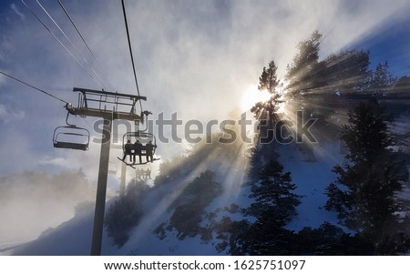 Group of friends on a snowboarding trip to Copper Mountain ride the chairlift through the fog on sunny winter morning. Morning sunbeams shine on snowboarders riding ski lift up to the top of mountain.
