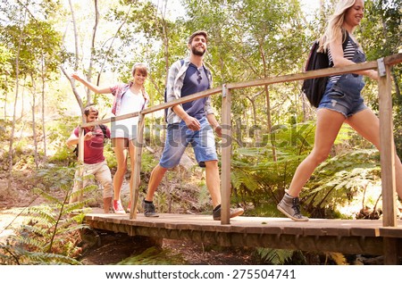 Group Of Friends On Walk Crossing Wooden Bridge In Forest