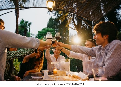 Group Of Friends Outside Eating And Have Fun Together Toasting With Red Wine Glasses At Sunset At Hotel Restaurant Where Are Staying - Cheerful People Laugh And Joke Evening At Sunset - Party At Home