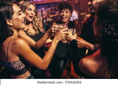 Group of friends partying in a nightclub and toasting drinks. Happy young people with cocktails at pub.