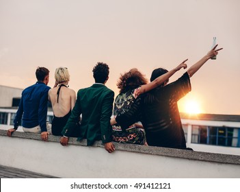 Group of friends partying on terrace with drinks. Young men and women enjoying drinks on rooftop at sunset. - Powered by Shutterstock