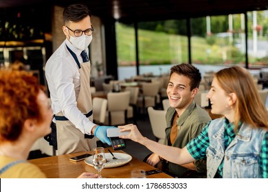 Group of friends paying contactless with mobile phone to a waiter in a cafe. Focus is on waiter. 