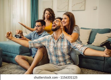 Group of friends play video games together at home, having fun. Celebrating victory. - Shutterstock ID 1156331125