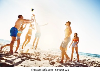 Group Of Friends Is Playing Beach Voleyball At Sunset Time