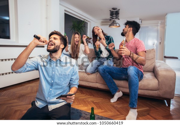 Group of friends playing karaoke\
at home. Concept about friendship, home entertainment and\
people