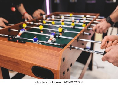 Group of friends playing kicker in a sports bar room, colleagues teammates play table football, table soccer game in the office, having fun, tabletop football match competition at work  - Powered by Shutterstock