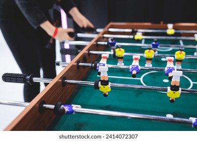 Group of friends playing kicker in a sports bar room, colleagues teammates play table football, table soccer game in the office, having fun, tabletop football match competition at work  - Powered by Shutterstock