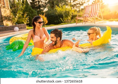 Group of friends at a poolside summer party,  having fun in the swimming pool, splashing water and fighting over a floating mattress - Powered by Shutterstock