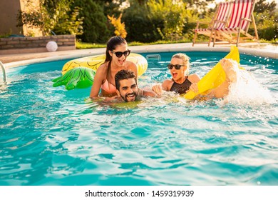 Group of friends at a poolside summer party,  having fun in the swimming pool, splashing water and fighting over a floating mattress - Powered by Shutterstock