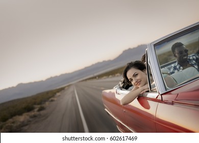 A Group Of Friends In A Red Open Top Convertible Classic Car On A Road Trip