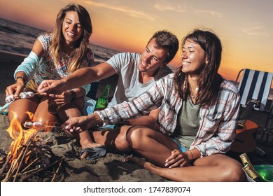 Group Of Friends Relaxing Around Bonfire On The Beach At Sunset