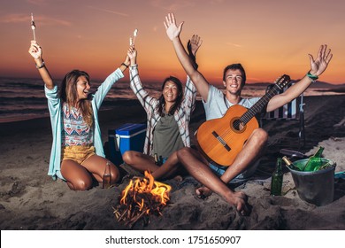 Group Of Friends Relaxing Around Bonfire On The Beach At Sunset