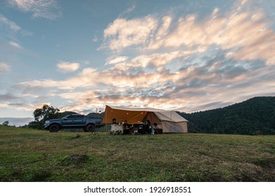 Group Of Friends Relaxing Inside Large Tent And Pickup Parked On Hill In Countryside At Camping Holiday