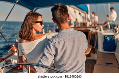 Group Of Friends Relaxing On Luxury Yacht. Having Fun Together While Sailing In The Sea. Romantic Couple Sitting Near Steering Wheel. Traveling And Yachting Concept.