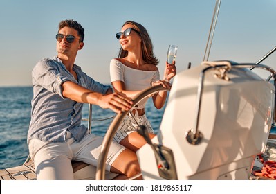 Group of friends relaxing on luxury yacht. Having fun together while sailing in the sea. Romantic couple sitting near steering wheel. Traveling and yachting concept.