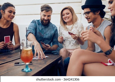Group of friends relaxing and playing cards together. Young people hanging out together around a table during a party playing a game of cards.