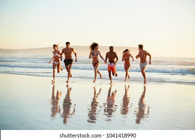 Group Of Friends Run Through Waves Together On Beach Vacation