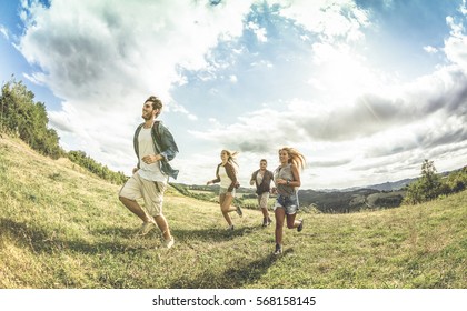 Group Of Friends Running On Grass Meadow - Friendship And Freedom Concept With Young Happy People Moving Free At Camping Experience - Vintage Desaturated Filter With Backlight Contrast Sunshine