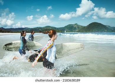 Group of friends running to the sea with surfboards having fun on the beach. - Powered by Shutterstock