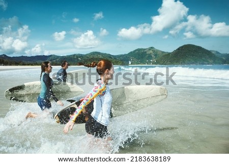 Group of friends running to the sea with surfboards having fun on the beach.