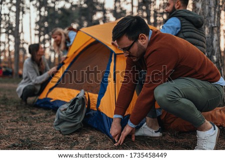 Group of friends setting up a tent while camping in the wilderness