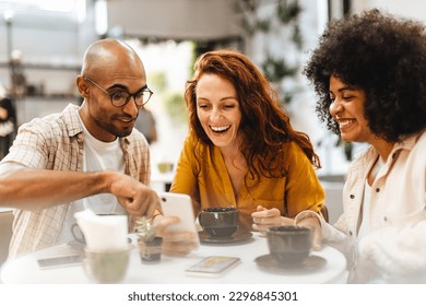 Group of friends sit together in a cafe, using a mobile phone to stay connected and share the latest news and updates. Happy young people socializing and having a good time over coffee. - Powered by Shutterstock