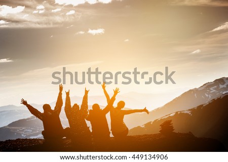 Group of friends sits on the top of mountain and having fun on mountains backdrop 