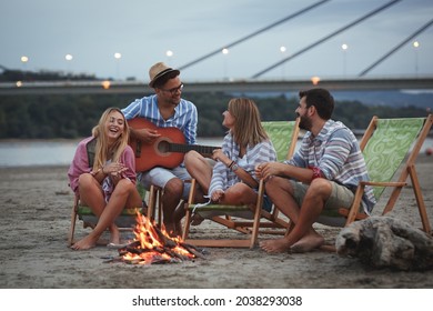 Group of friends sitting around camp fire at the beach at the autumn evening.They play guitar and singing.	
 - Powered by Shutterstock