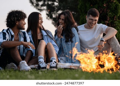 Group of friends sitting around the fire in evening, talking, laughing and having a great time outdoor.  - Powered by Shutterstock