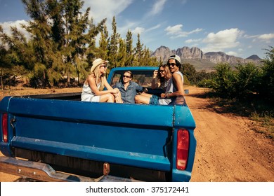 Group of friends sitting at the back of a pick up car. Young men and women going on a road trip in nature.