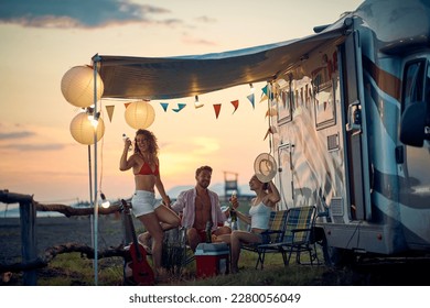 A group of friends is sitting in the camp and drinking on a beautiful sunset. Vacation, friendship, camping, nature - Powered by Shutterstock