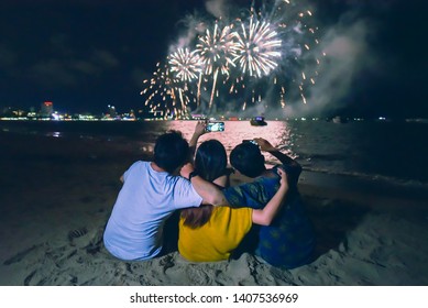 Group Of Friends Sitting And Holding Each Others Enjoy Watching Fireworks Display On The Beach