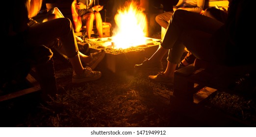 The group of friends are sitting near the bonfire in the night and talking about something