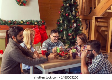 Group of friends sitting on the living room floor next to a nicely decorated Christmas tree on a Christmas morning, drinking coffee and having fun - Powered by Shutterstock