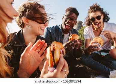 Group of friends sitting on mountain top eating burger. Excited young men and women enjoying and partying outdoors. - Powered by Shutterstock