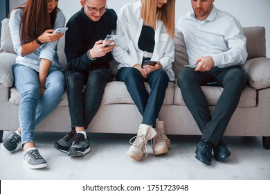 Gruppe von Freunden, die zusammen auf dem Sofa mit Handys sitzen.