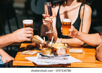 Group Of Friends Sitting On A Summer Terrace With Beer And Wine In Their Hands And Snacks On The Table