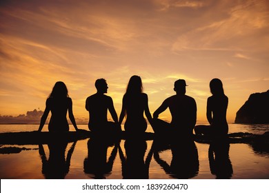 Group of friends are sitting at sea beach and enjoys sunset