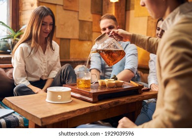 Group of friends sitting at the table and looking at delicious hot drink while man performing tea ceremony - Powered by Shutterstock