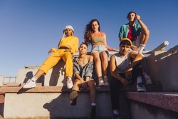 Group Of Friends Sitting Together Outdoors In The Sun. Multiethnic Youngsters Spending Quality Time Together In The City. Group Of Generation Z Friends Chilling Outdoors.