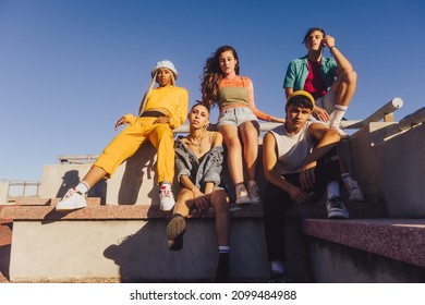 Group Of Friends Sitting Together Outdoors In The Sun. Multiethnic Youngsters Spending Quality Time Together In The City. Group Of Generation Z Friends Chilling Outdoors.