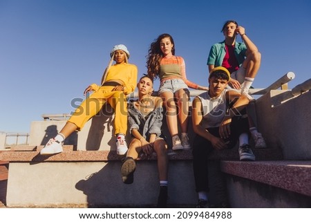 Group of friends sitting together outdoors in the sun. Multiethnic youngsters spending quality time together in the city. Group of generation z friends chilling outdoors.