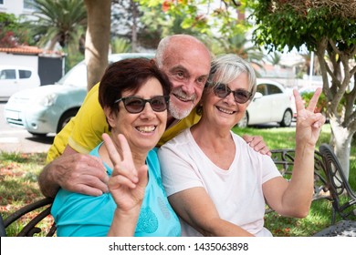 Group Of Friends Smiling Sitting In A Bench At The Park. Green Garden, Summer Day. Three Caucasian Senior Peoples Gesturing Message Everything Is Ok.