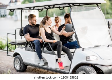 Group Of Friends In Sports Wear Having Fun Driving A Golf Cart Near The Lake