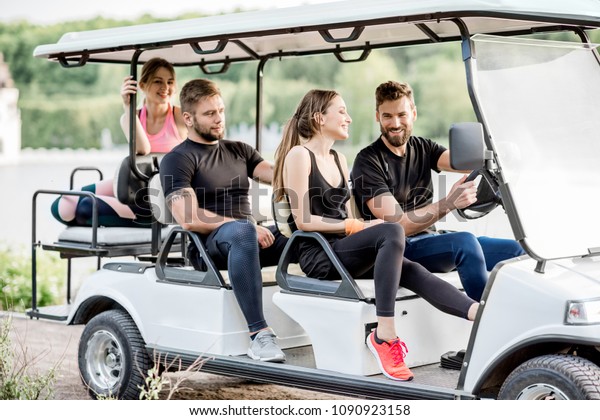Group of friends in sports wear having fun driving a\
golf cart near the lake