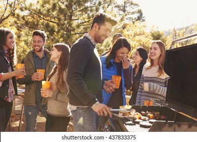 Group of friends stand at a barbecue, one cooking at grill - Powered by Shutterstock