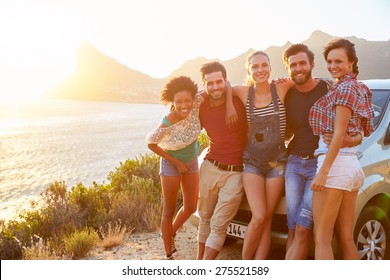 Group Of Friends Standing By Car On Coastal Road At Sunset